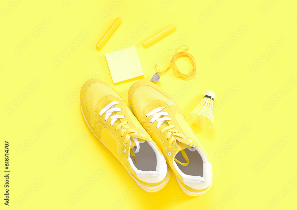 Sneakers with whistle, shuttlecock and stationery on yellow background