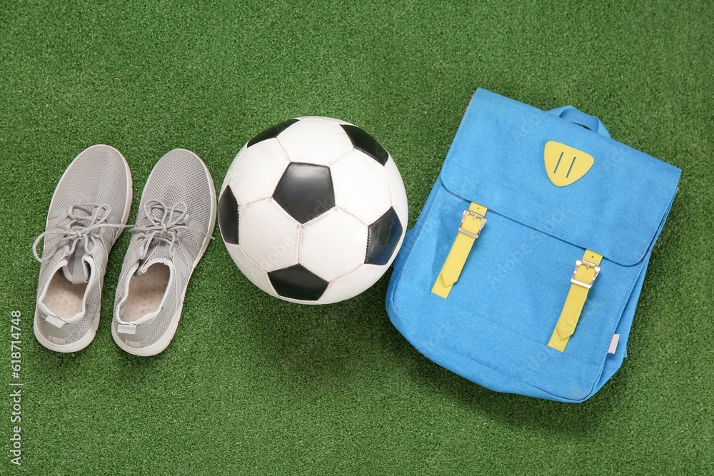 Sneakers with backpack and soccer ball on color background