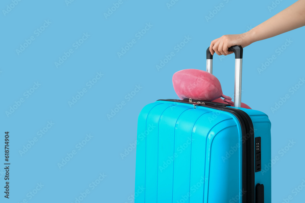 Female hand with suitcase and travel cushion on blue background. Travel concept