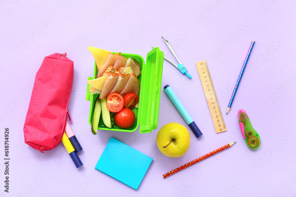 Different stationery and lunch box with tasty food on lilac background