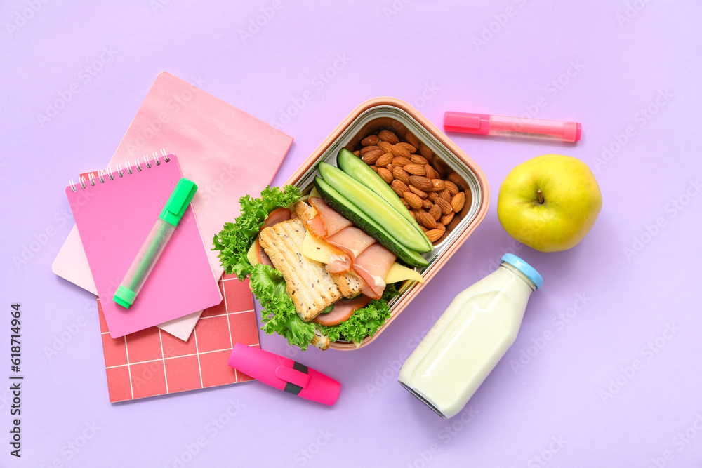 Stationery, drink and lunch box with tasty food on lilac background