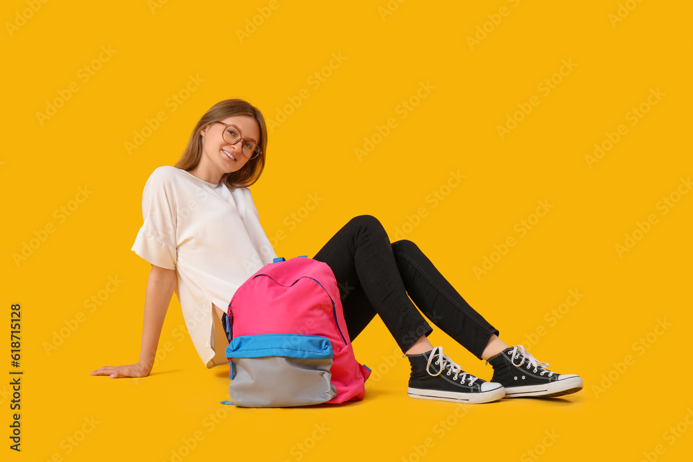 Female student with backpack sitting on yellow background