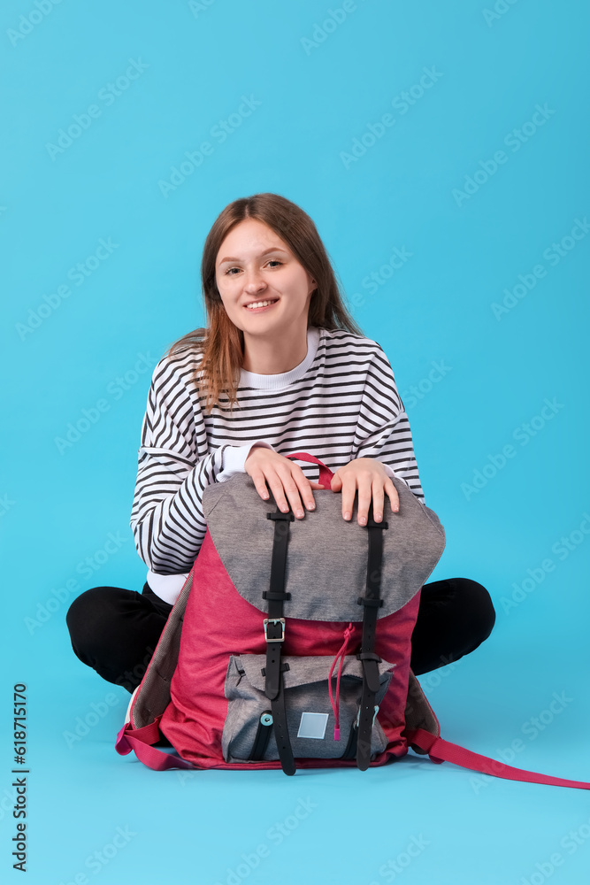 Female student with backpack sitting on blue background