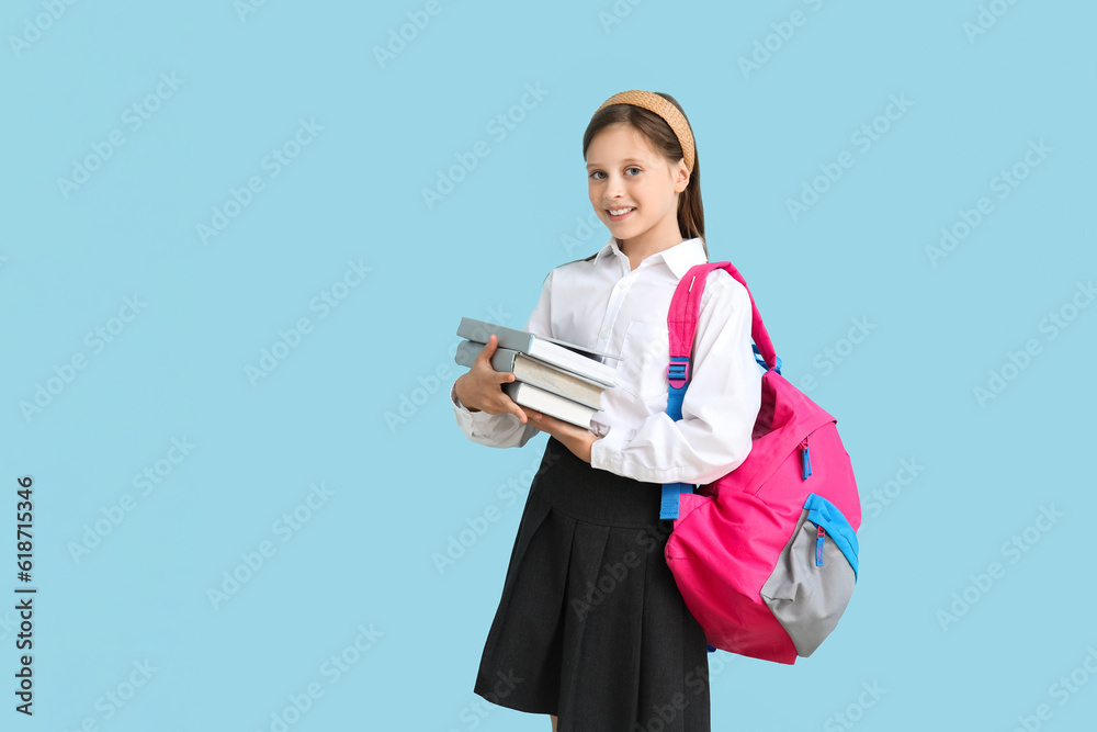 Little schoolgirl with books and backpack on blue background