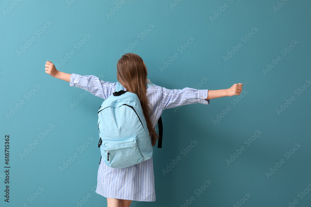 Little schoolgirl with backpack on blue background, back view