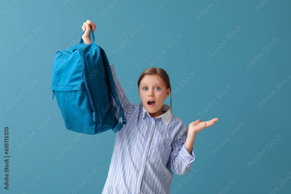 Shocked little schoolgirl with backpack on blue background