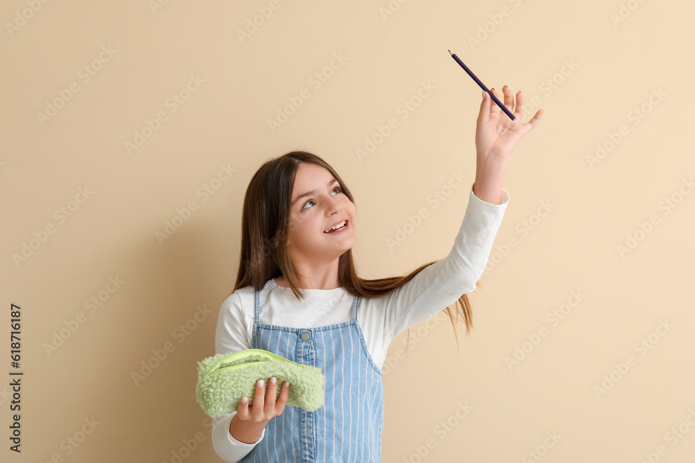 Little girl with pencil case on beige background