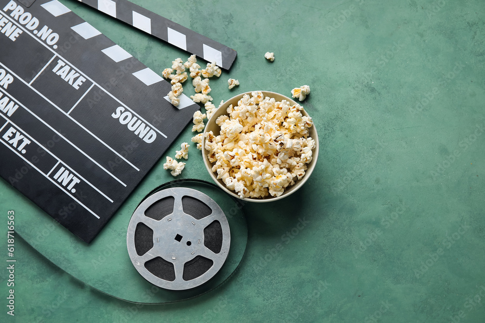 Bowl with tasty popcorn, clapperboard and film reel on green background