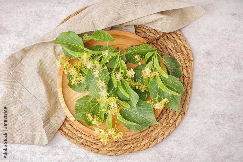 Wooden plate with branches of linden flowers on light background