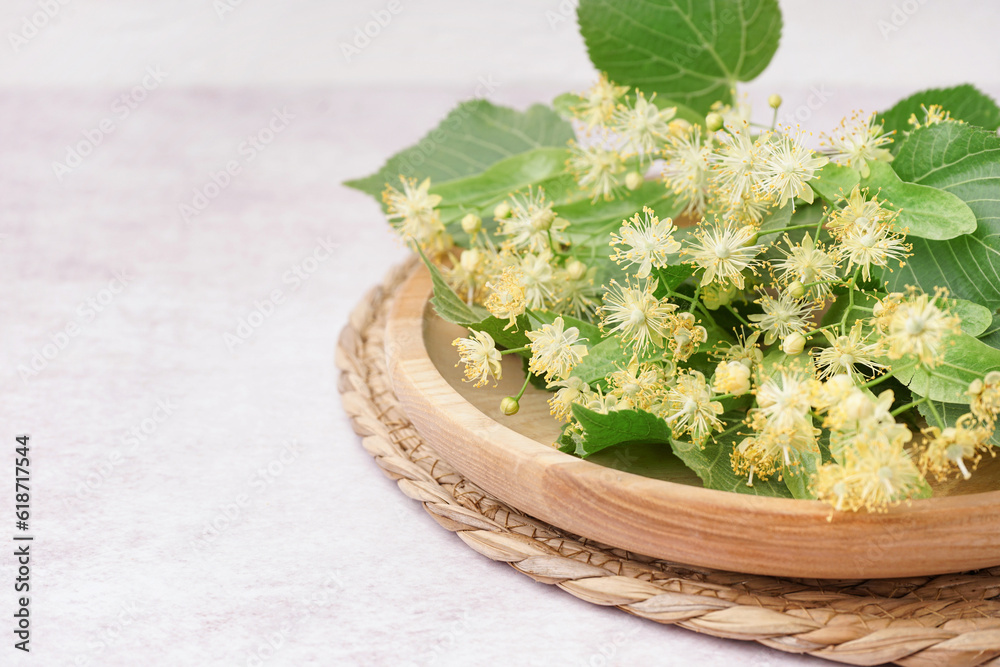 Wooden plate with branches of linden flowers on light background