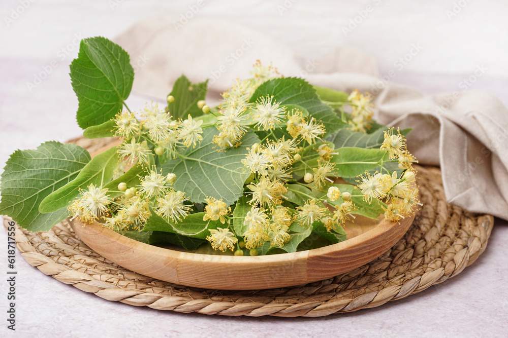 Wooden plate with branches of linden flowers on light background