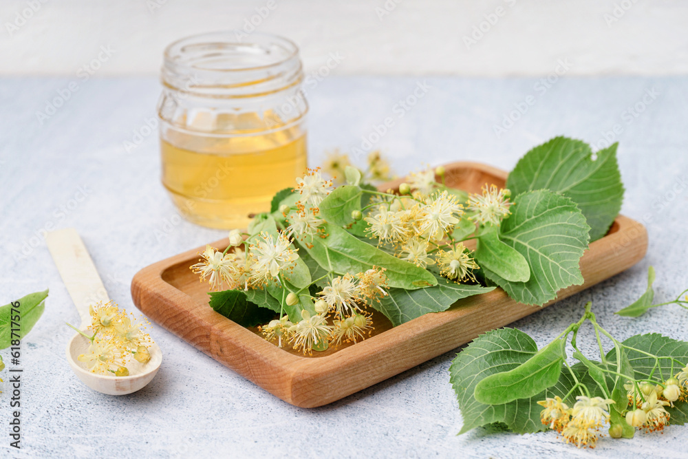 Wooden board with fresh linden flowers and honey on light background