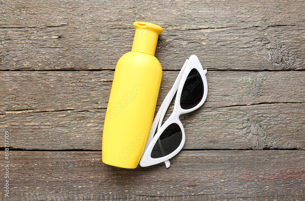 Sunglasses with bottle of sunscreen cream on brown wooden background