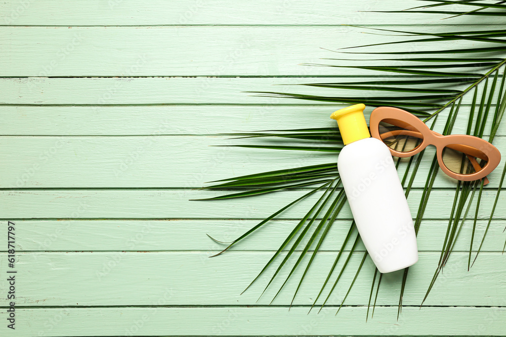 Sunglasses with bottle of sunscreen cream and palm leaf on green wooden background