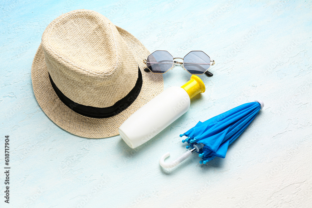 Wicker hat with sunglasses, mini umbrella and bottle of sunscreen cream on gradient background