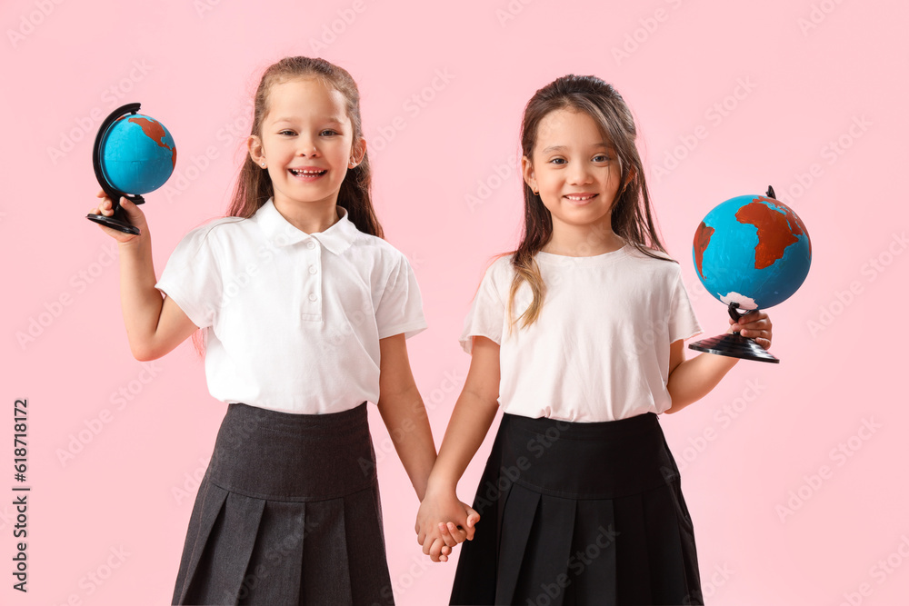 Little schoolgirls with globes on pink background