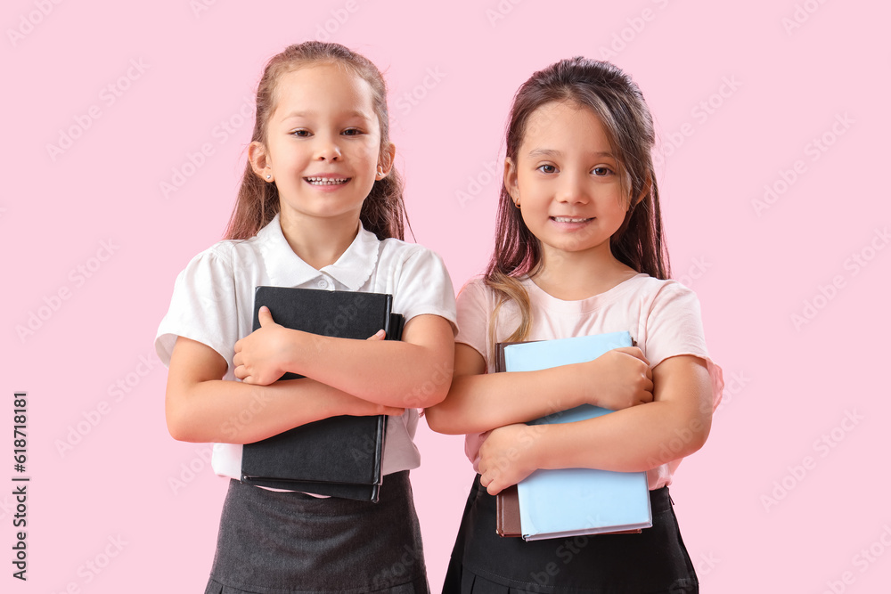 Little schoolgirls with books on pink background