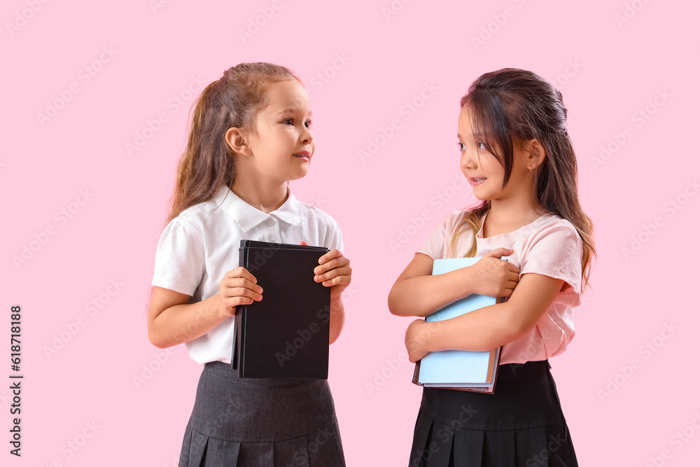 Little schoolgirls with books on pink background