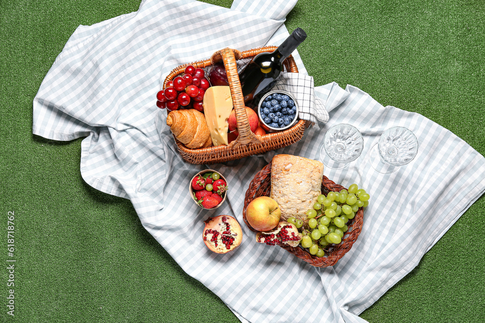 Wicker basket with tasty food for picnic, wine and glasses on green background