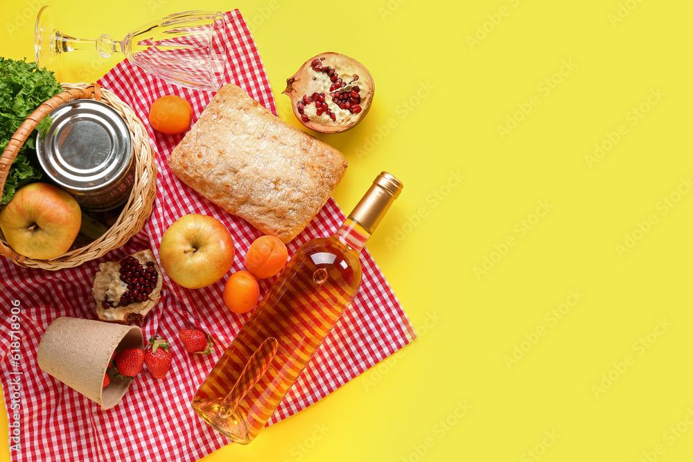 Wicker basket with tasty food for picnic, wine and glass on yellow background