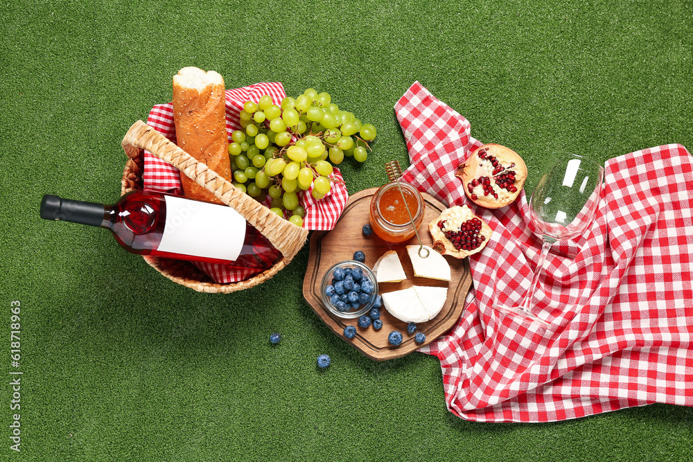 Composition with tasty food for picnic, honey and bottle of wine on green background