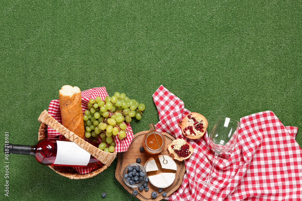 Composition with tasty food for picnic, honey and wine on green background