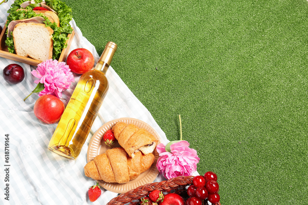 Composition with tasty food for picnic, wine and peony flowers on green background