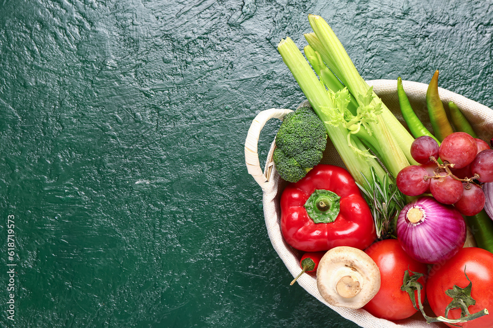 Wicker basket with fresh ripe vegetables on green background