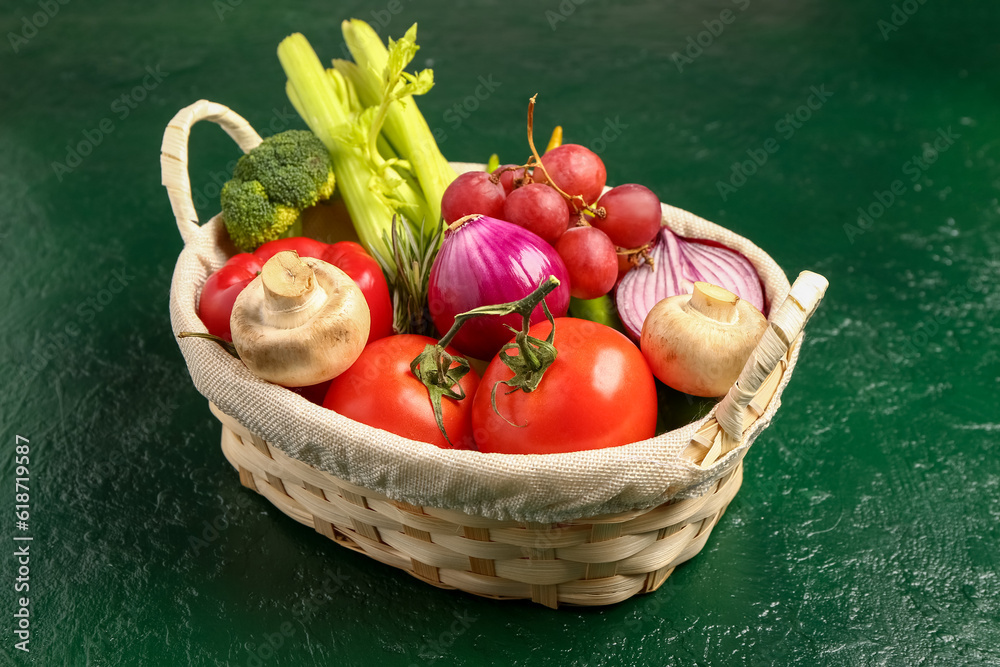 Wicker basket with fresh ripe vegetables on green background, closeup