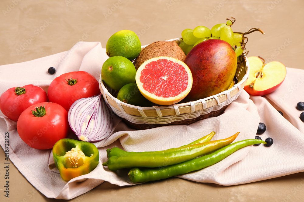 Wicker bowl with different fresh fruits and vegetables on brown background