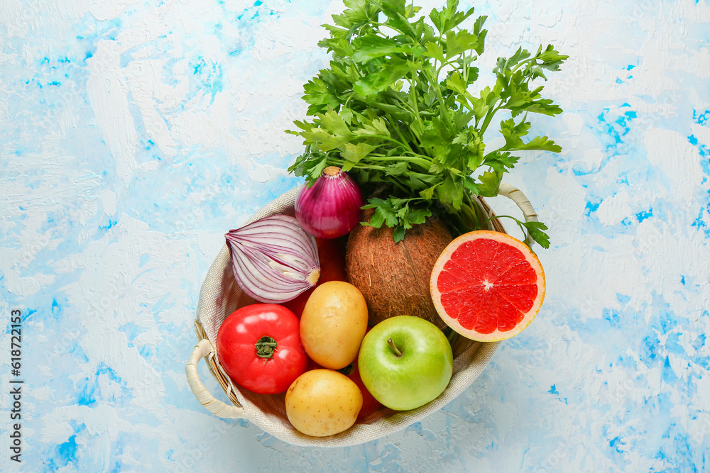 Wicker basket with different fresh fruits and vegetables on blue background