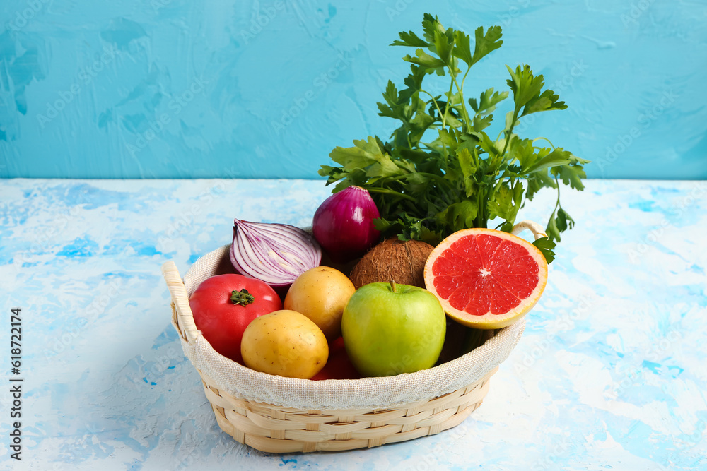 Wicker basket with different fresh fruits and vegetables on blue background