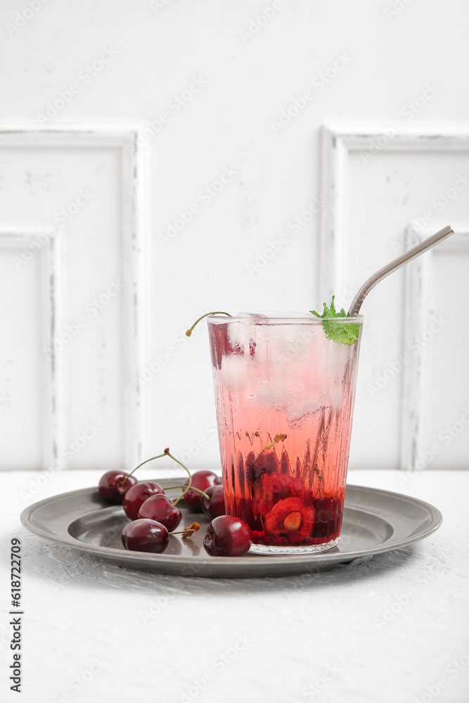 Glass of tasty cherry lemonade and plate with berries on white background