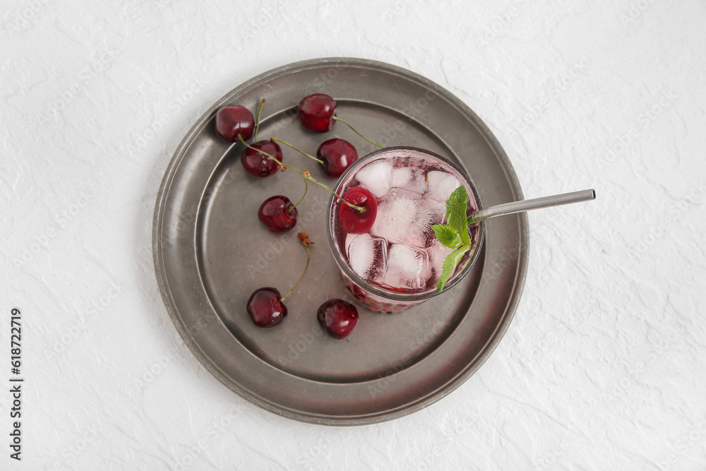 Glass of tasty cherry lemonade and plate with berries on white background