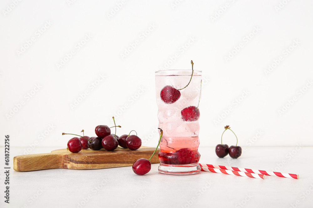 Glass of tasty cherry lemonade and wooden board with berries on white background