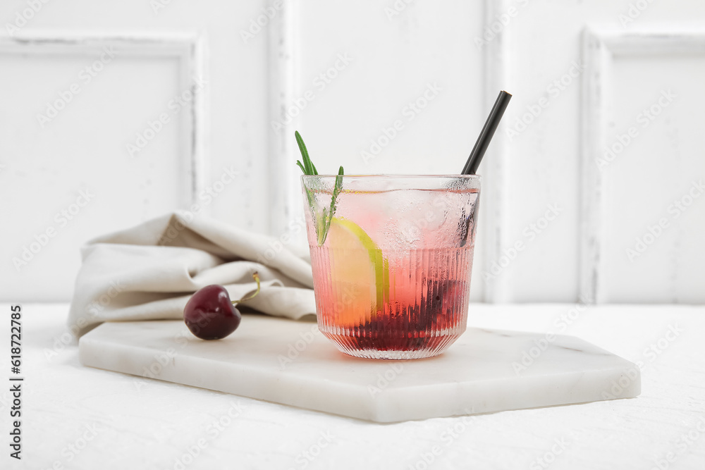 Board with glass of tasty cherry lemonade and rosemary on white background