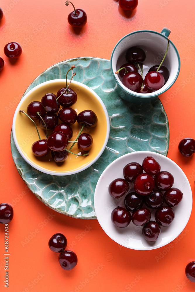 Plates and cup with sweet cherries on orange background