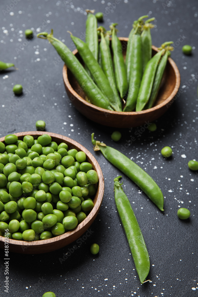 Bowls with fresh green peas on black background