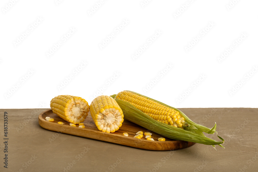 Wooden board with fresh corn cobs and seeds on brown table against white background