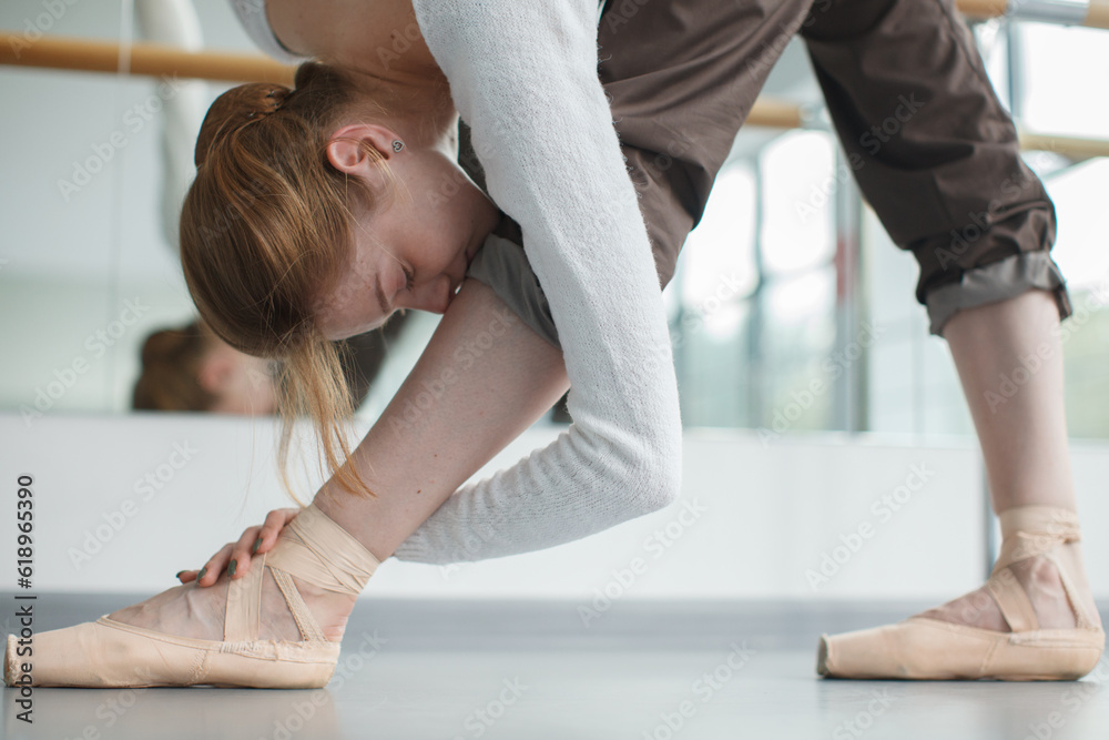 young ballerina doing ballet exercise bowing to feet with pointe shoes in choreography class