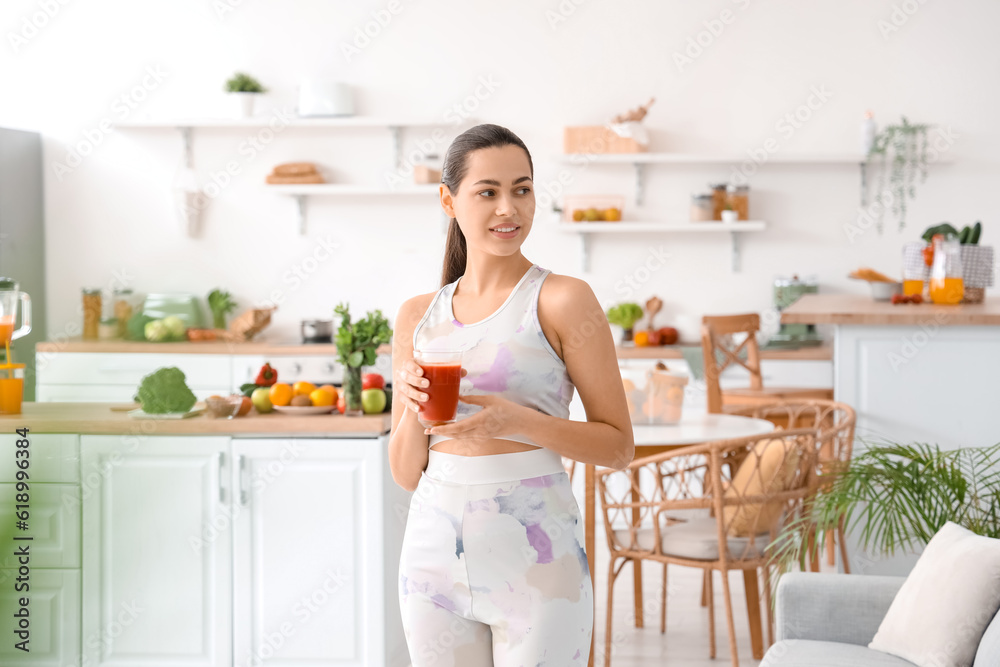 Sporty young woman with glass of vegetable juice in kitchen