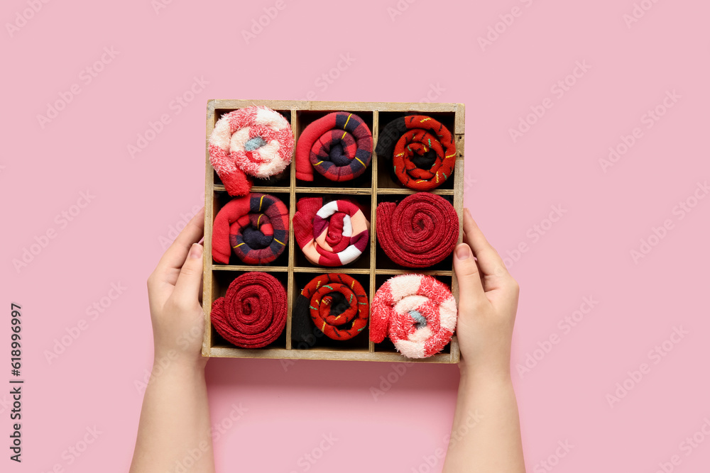 Female hands with box of different socks on pink background