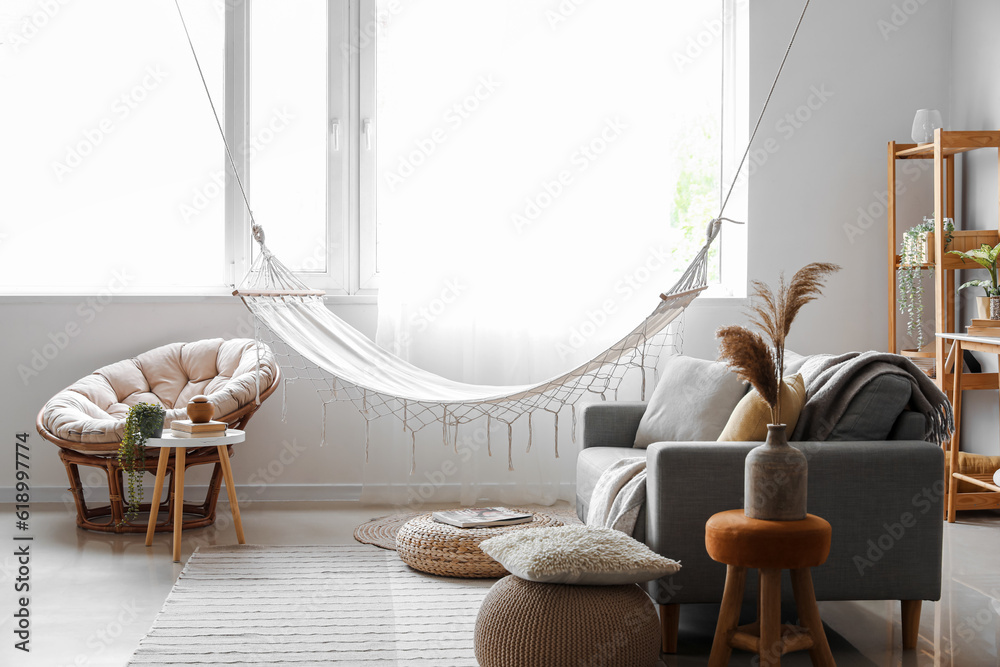 Interior of light living room with hammock, grey sofa and armchair