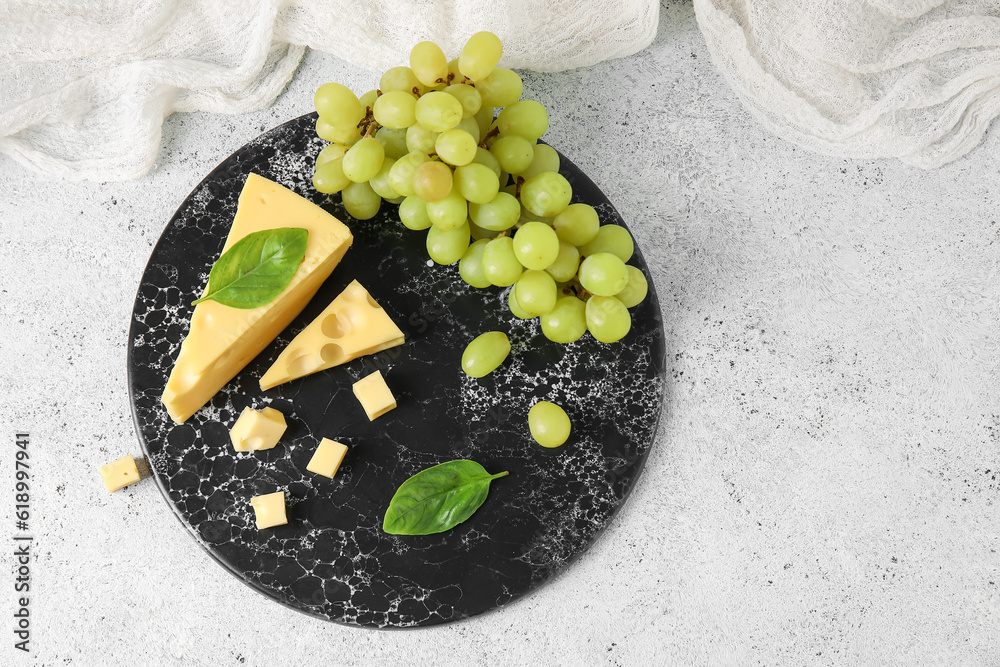 Board with tasty Swiss cheese and grapes on light background