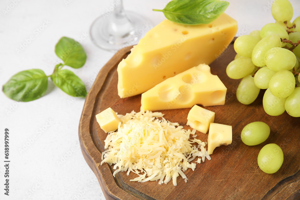 Wooden board with tasty Swiss cheese and grapes on light background