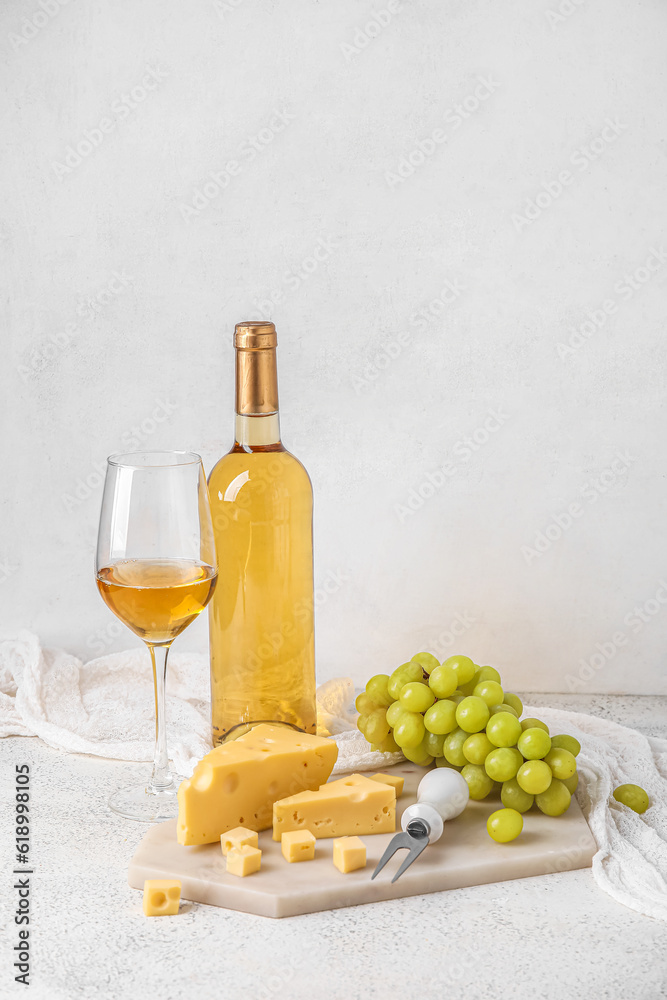 Board with tasty Swiss cheese, glass and bottle of wine on light background