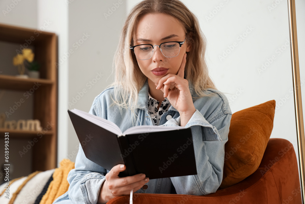 Young woman in stylish eyeglasses reading book at home, closeup