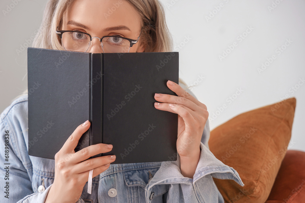 Young woman in stylish eyeglasses reading book at home, closeup