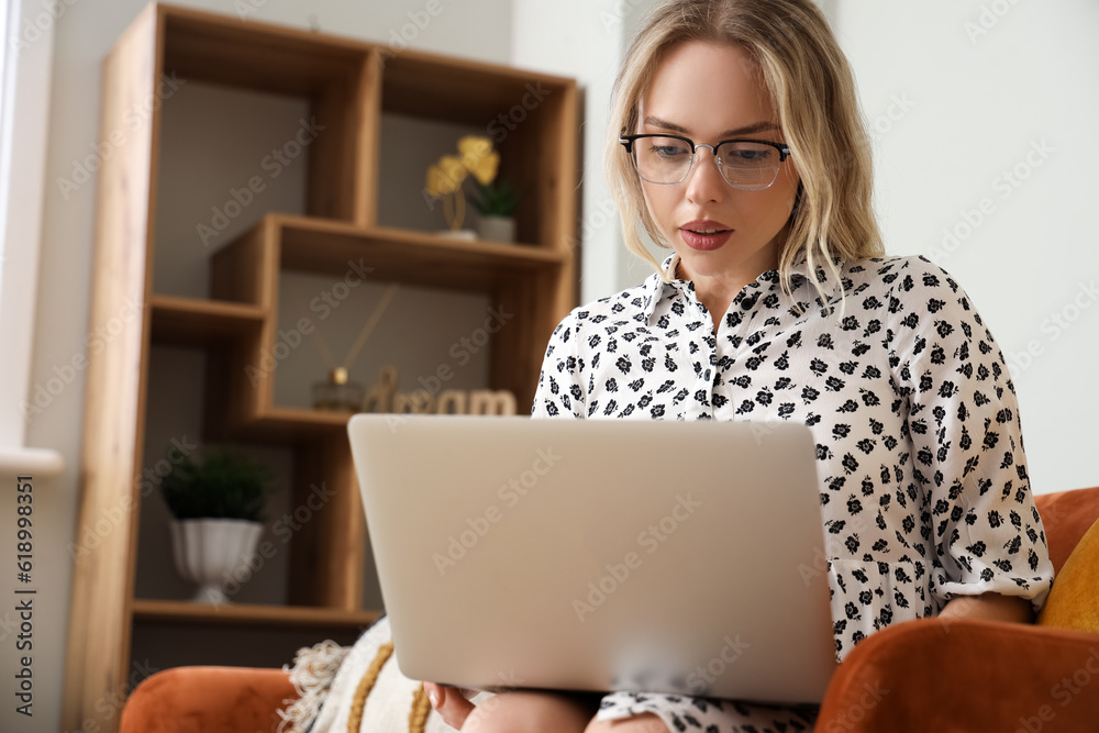 Young woman in stylish eyeglasses using laptop at home