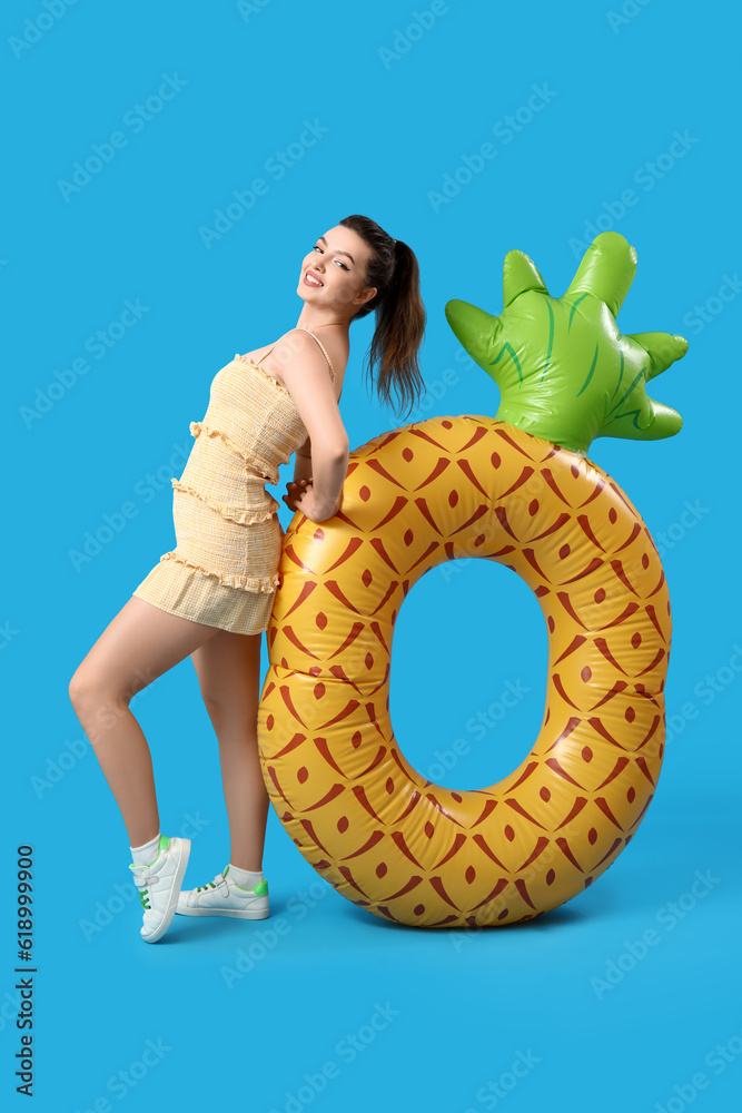 Young woman with swim ring in shape of pineapple on blue background